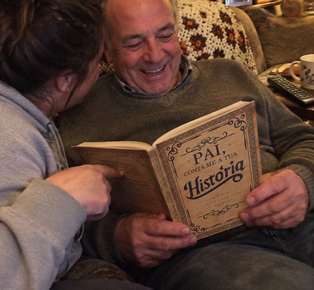 Pai a rir no sofá com o livro Pai, conta-me a tua História